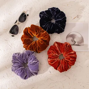 Top view of four elegant velvet scrunchies in navy, brown, purple and rust orange