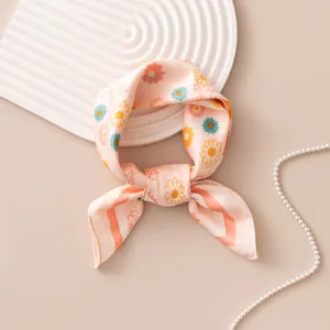 Detailed view of a pink floral silk square scarf tied into an elegant bow on a beige background