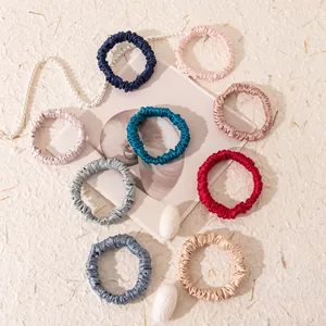 Set of multicolored 1cm mulberry silk scrunchies arranged on a cream textured background.