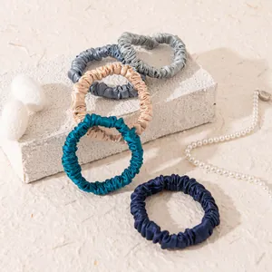 Detailed view of five mulberry silk scrunchies in assorted colors on stone texture background.