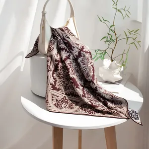 Élégant foulard en soie et laine marron à motif cachemire sur un sac blanc sous la lumière