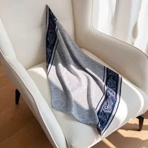 Détail d'un carré en laine et soie à motif cachemire drapé sur un fauteuil blanc moderne