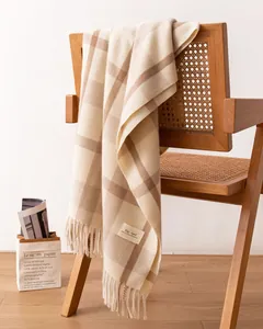 Close-up of a soft beige plaid scarf with fringe draped on a rustic wooden chair.