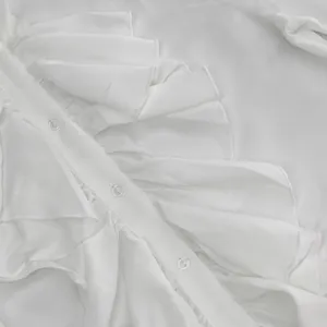 Primer plano de una blusa blanca con volantes elegantes y botones transparentes.
