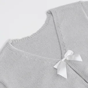 Close-up detail of a grey knitted sweater featuring a white satin bow and V-neckline