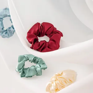 Detailed view of soft silk scrunchies in various elegant colors on draped white fabric.