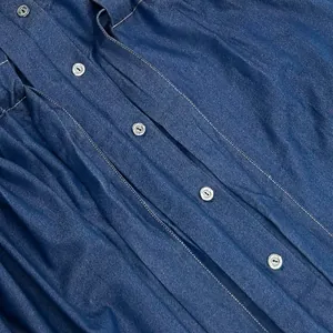 Macro detail view of engraved metal buttons and blue denim fabric on midi dress.