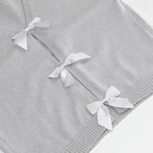 Detailed view of elegant white satin ribbon bows on soft grey knitted sweater texture