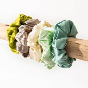 Detail of five silk satin scrunchies in pastel colors on a natural wood branch.