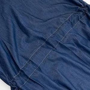 Close-up of blue denim fabric with white stitching details on a long dress.