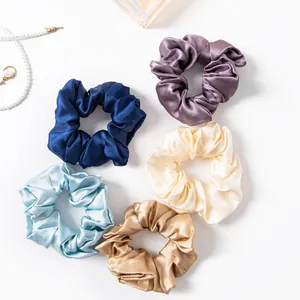 Set of five colorful silk satin scrunchies with elegant sheen on white background.