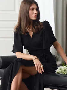 Elegant black short-sleeved wrap dress detail shown on female model sitting on sofa