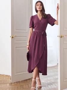 Elegant short-sleeved wrap dress in deep purple standing between classic white doors.