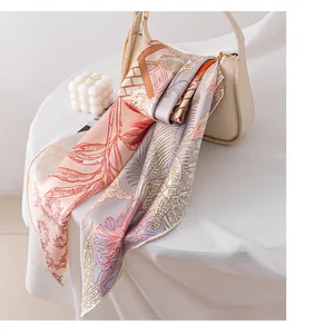 Elegant floral silk scarf draped over a beige handbag in a bright, modern setting.