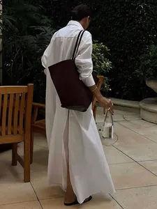 Back view of a long white French-style shirt dress with a stylish back slit in a garden