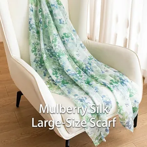Elegante sciarpa lunga in seta di gelso con stampa floreale verde drappeggiata su sedia bianca.