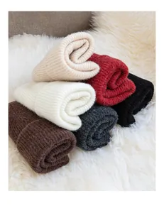 Detailed view of several colorful wool knit beanies on a soft white plush background
