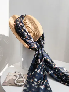 Close-up detail of navy floral mulberry silk scarf tied around a summer straw hat