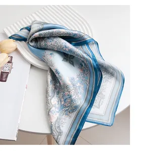 Elegant light blue silk square scarf with intricate floral paisley patterns on white tray