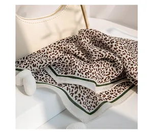 Close-up of leopard print silk scarf with white green border and decorative pom-poms
