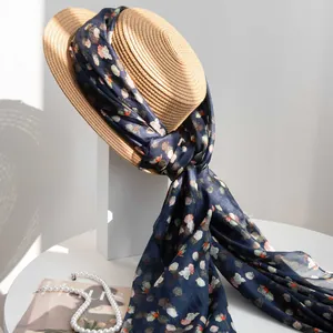 Elegant navy blue floral mulberry silk scarf wrapped on a stylish straw hat.