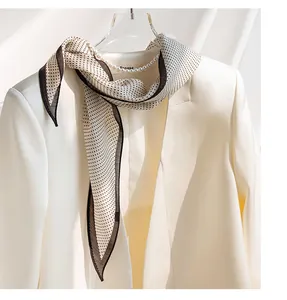 Dettaglio di un elegante foulard di seta a pois su un blazer bianco con perle.