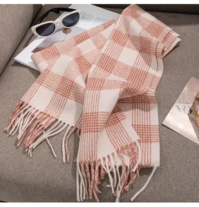Detail shot of a soft pink plaid wool scarf with fringes displayed on a cozy beige sofa