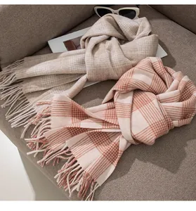 Detail view of soft pink and beige plaid wool scarves with tassels on a tan sofa.