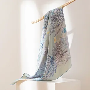 Elegante sciarpa in seta di gelso con stampe botaniche drappeggiata su un ramo di legno.