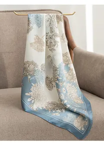Elegant blue floral silk-like square scarf draped on a gold hanger over a sofa.