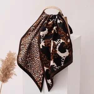 Elegant leopard print silk wool scarf draped over a cream bag on a white pedestal.