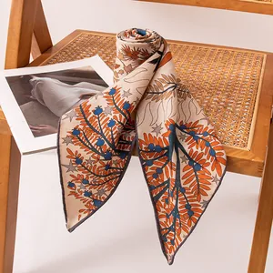 Elegant silk and wool triangle scarf with orange and blue botanical print on rattan chair.