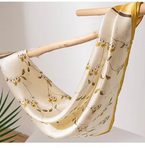 Detailaufnahme eines Maulbeerseidenschals mit gelbem Blumenmuster an einem Holzast.