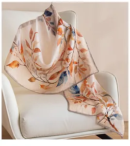 Luxury silk scarf with autumn leaf pattern draped on a modern white chair.