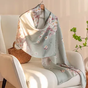 Elegant long silk scarf with cherry blossom floral print draped on a modern white chair.