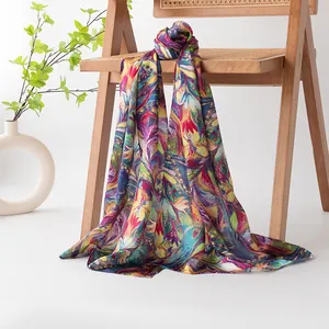 Elegant long silk scarf with colorful phoenix feather print draped on a wooden chair