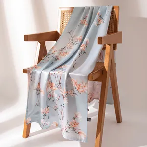 Luxurious light blue mulberry silk scarf with elegant floral print draped over a wooden chair