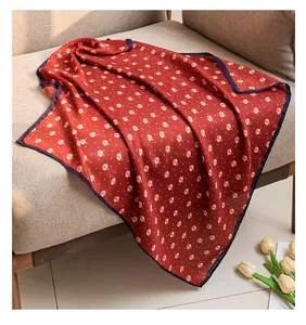 Red pastoral style silk scarf with small white leaf print draped on a cozy grey sofa