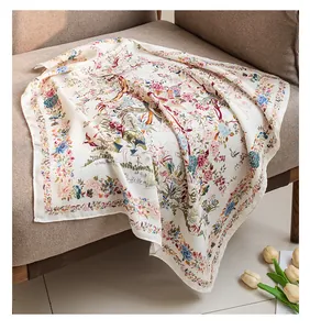 Detailed view of a beige silk-like square scarf with floral print draped on a sofa.
