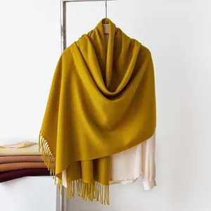 Detail view of a mustard yellow cashmere-like scarf with fringe draped over a hanger