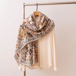 Exotic floral silk wool scarf draped elegantly over a neutral blouse on a wooden hanger.