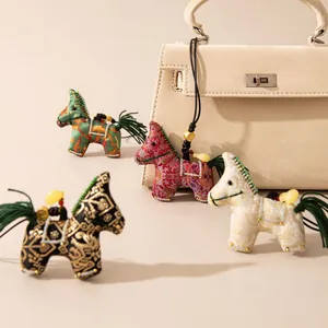 Four Chinese style Song brocade silk horse charms displayed with a luxury beige handbag prop