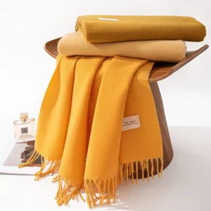 Close-up of elegant mustard yellow cashmere-like scarf with fringe detail on a wooden stool