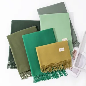 Detailed view of elegant solid color cashmere-like scarves with fringe in green tones