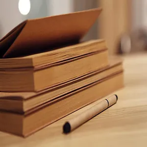 Detail shot of stacked retro kraft paper sketchbooks with a pencil on a desk.