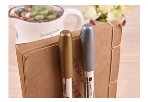 Detailed view of gold and silver metallic paint markers clipped to a kraft notebook