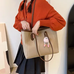 Close-up of a vintage khaki tote bag with brown straps and a pink plush charm.