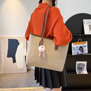 Large beige vintage tote bag with pink fuzzy keychain shown on model shoulder in a cozy setting