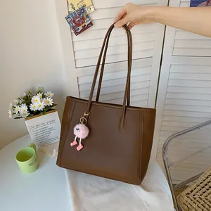 Detail shot of a brown vintage tote bag featuring a pink fluffy charm held by hand