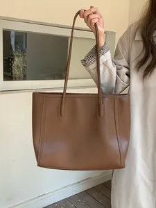 Close-up detail of a vintage brown large capacity leather tote bag held by a fashion model